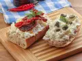 Dwa kawałki bagietki z twarogiem, suszonymi pomidorami i kaparami. Kapary dodają wyrazistego smaku, świetnie komponując się z serem i pomidorami.