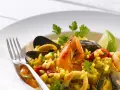 Pyszne risotto z owocami morza: krewetki, małże, kalmary i ryż, udekorowane natką pietruszki i ćwiartką limonki.