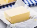 Kostka masła na papierze, obok niebiesko-biała kratka. Czy masło można mrozić? Tak, można je zamrozić.