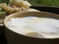 Domowy sposób na zsiadłe mleko. Gęste, białe zsiadłe mleko w glinianej miseczce, obok ziemniaki z koperkiem.
