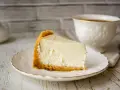 Pyszny sernik z mlekiem skondensowanym na kruchym spodzie, podany na talerzyku z filiżanką kawy.