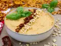 Aksamitny hummus z suszonymi pomidorami i orzeszkami pinii, udekorowany listkami bazylii. Idealny do chrupiących precelków.