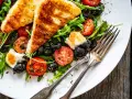 Pyszna sałatka z grillowanym halloumi, pomidorkami koktajlowymi i czarnymi oliwkami, podana na talerzu z widelcami.