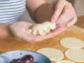 Ręce formują pierogi ruskie na drewnianej desce. W tle miska z wiśniami.