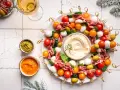 Kolorowe przystawki na zimno w kształcie wieńca, z mozzarellą, pomidorkami, oliwkami i salami, podane z dipami.