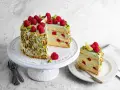 Wyjątkowy tort pistacjowo malinowy, udekorowany świeżymi malinami i pistacjami. Kawałek ciasta na talerzyku kusi warstwami biszkoptu i kremu.