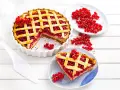 Pyszna tarta z porzeczkami, z kratką z ciasta i świeżymi owocami na wierzchu. Obok kawałek ciasta na talerzyku.