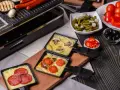 Raclette z pieczarkami i pomidorami, obok kiełbaski. Idealny ser do raclette rozpuszcza się w tych małych patelenkach.