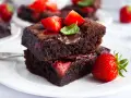 Pyszne brownie z truskawkami, polane czekoladą i ozdobione listkiem mięty. Idealne na deser.