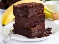 Stos puszystych brownie z bananami, ozdobiony ziarnami kawy, na talerzu z widocznym bananem w tle.
