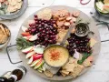 Idealne menu na sylwestra w domu: deska z serkiem, winogronami, jabłkami, kiełbaską i krakersami.