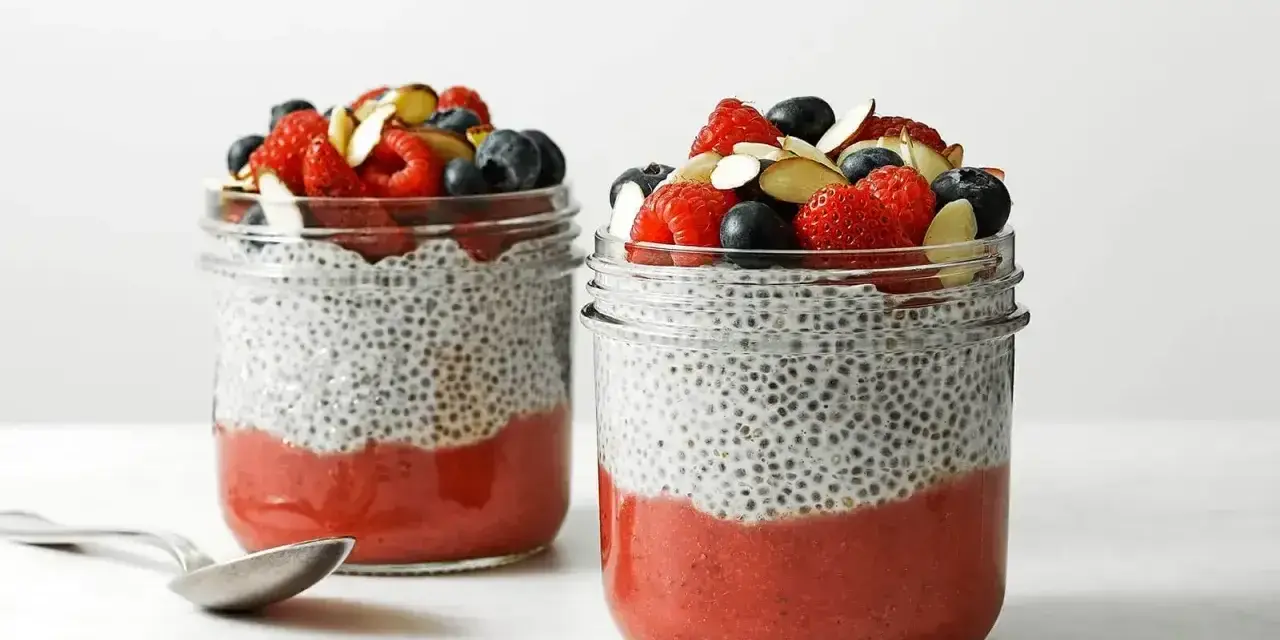 Pyszny pudding chia przepis: warstwy musu truskawkowego i nasion chia, zwieńczone świeżymi owocami i migdałami.