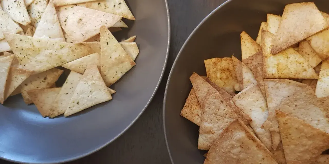 Dwa talerze pełne chrupiących chipsów z tortilli, jedne z ziołami, drugie z przyprawami. Idealne na przekąskę!