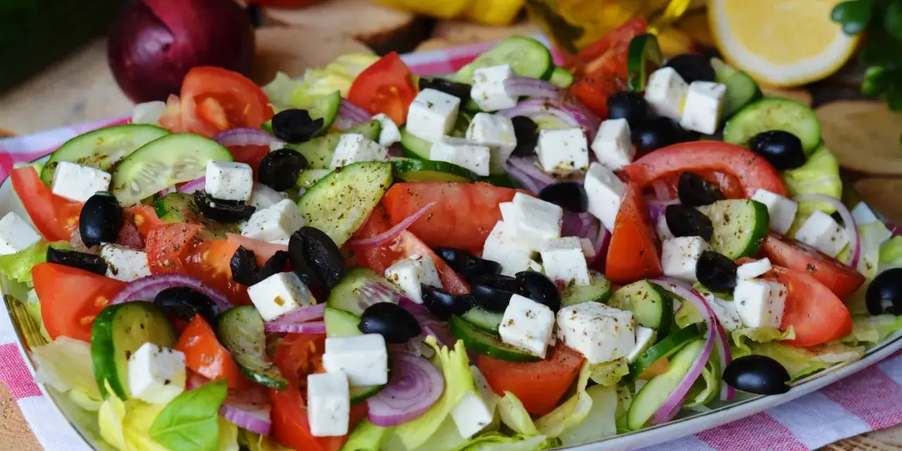 Pyszna sałatka grecka z pomidorami, ogórkiem, fetą, oliwkami i czerwoną cebulą, skropiona oliwą.