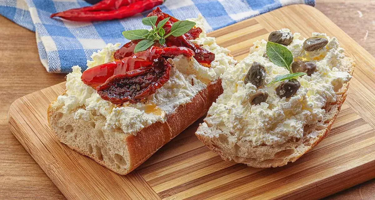 Dwa kawałki bagietki z twarogiem, suszonymi pomidorami i kaparami. Kapary dodają wyrazistego smaku, świetnie komponując się z serem i pomidorami.