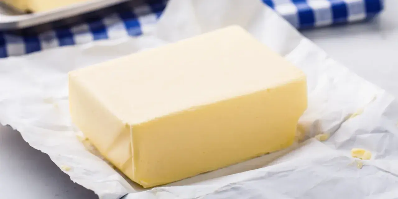 Kostka masła na papierze, obok niebiesko-biała kratka. Czy masło można mrozić? Tak, można je zamrozić.