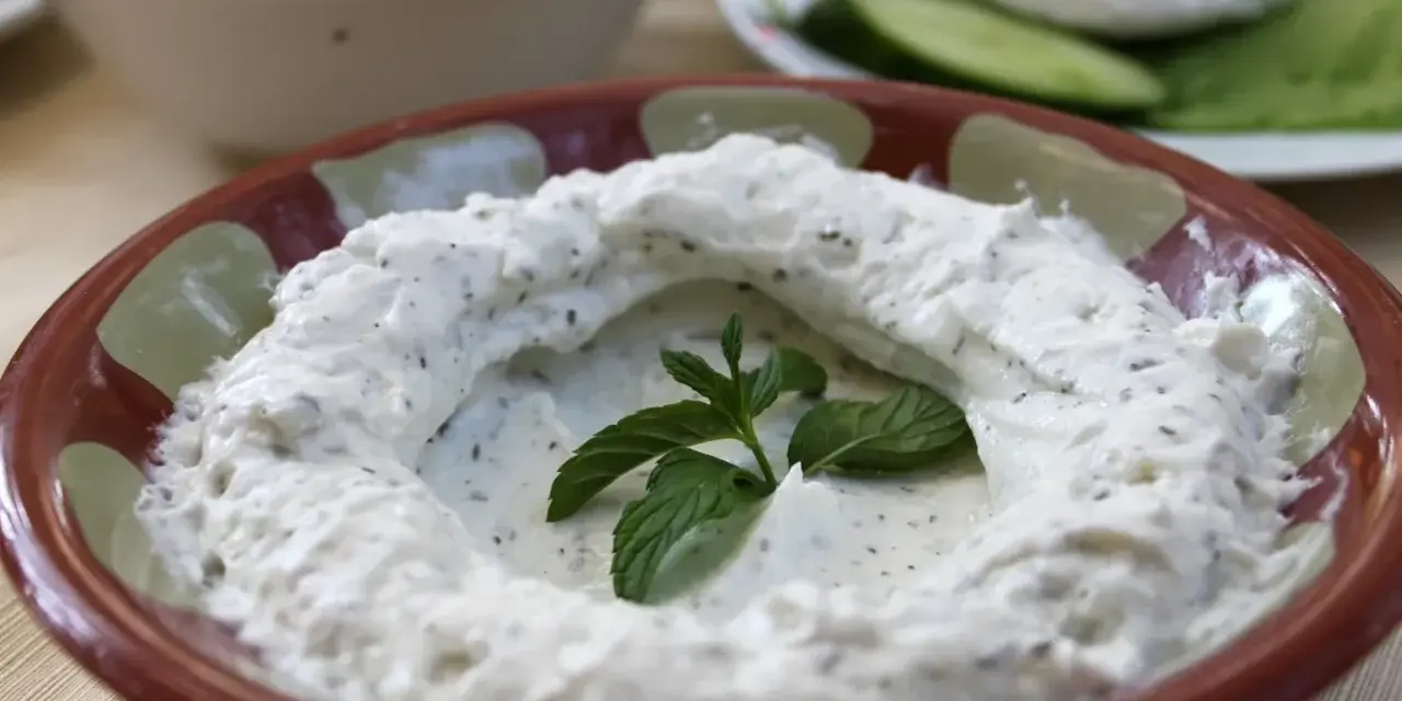 Kremowy labneh co to? Gęsty, biały serek z ziołami, udekorowany świeżą miętą, w glinianej misce.