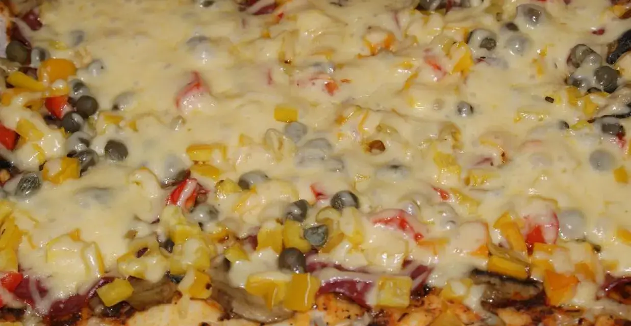 Pyszna pizza na grubym cieście z warzywami i roztopionym serem.