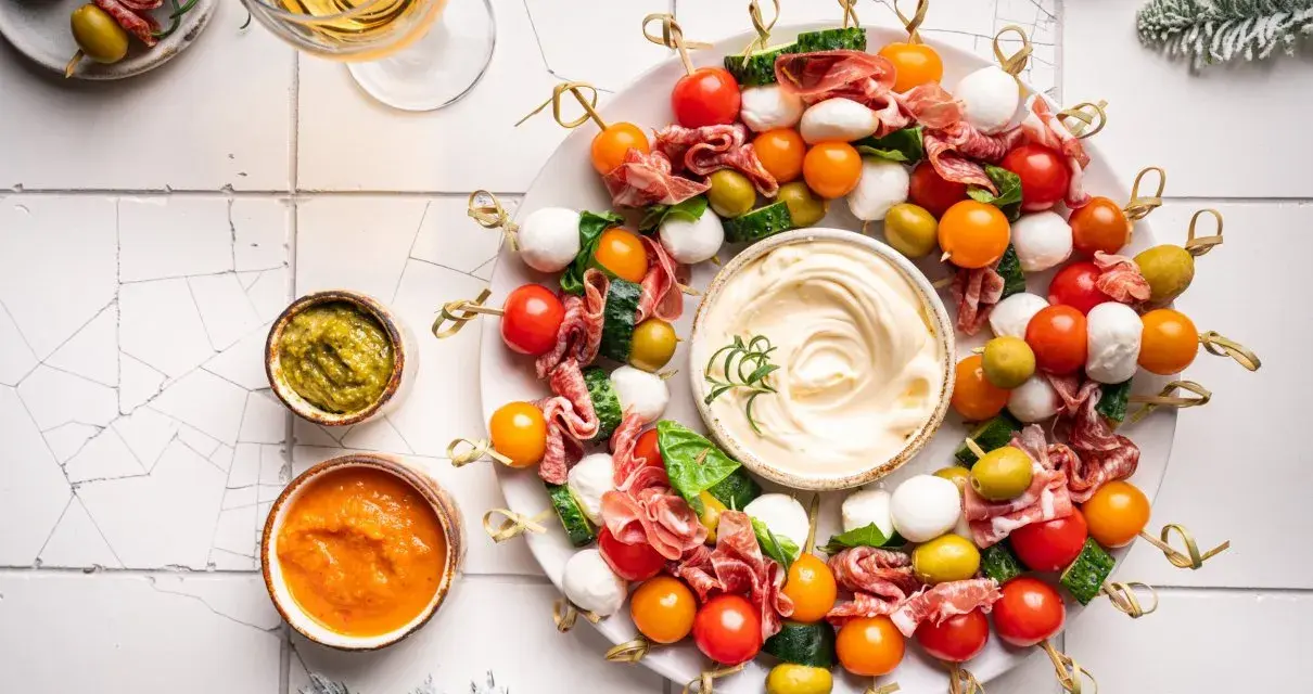 Kolorowe przystawki na zimno w kształcie wieńca, z mozzarellą, pomidorkami, oliwkami i salami, podane z dipami.