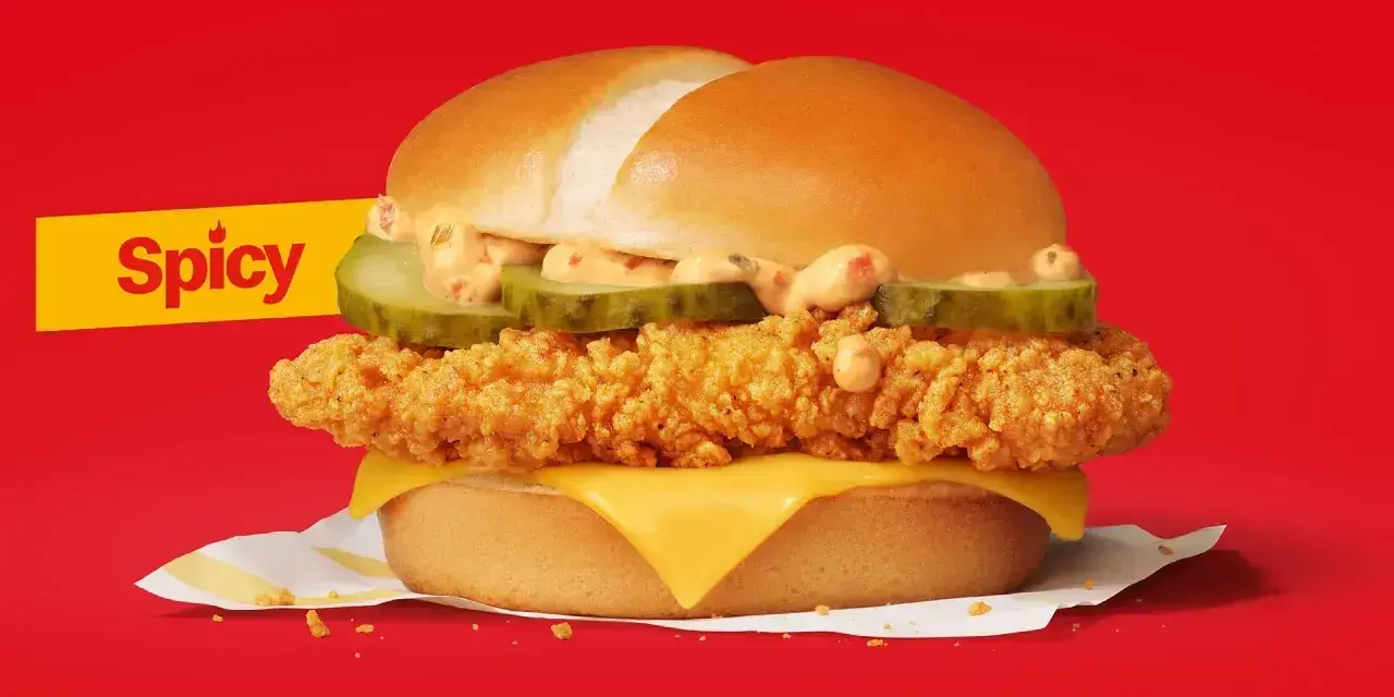 Pikantna kanapka z kurczakiem, z chrupiącym kotletem, serem, ogórkiem i kremowym sosem, na tle w kolorze czerwonym.