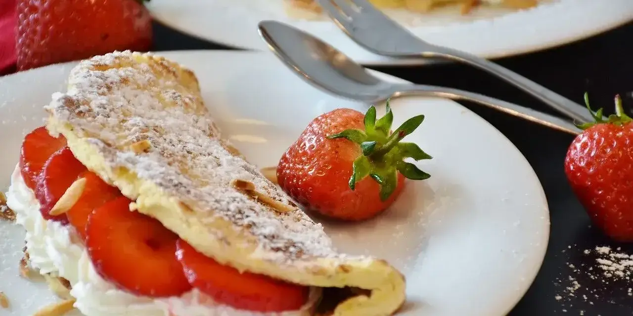 Słodki omlet z bitą śmietaną i truskawkami, posypany cukrem pudrem. Idealny przepis na deser.