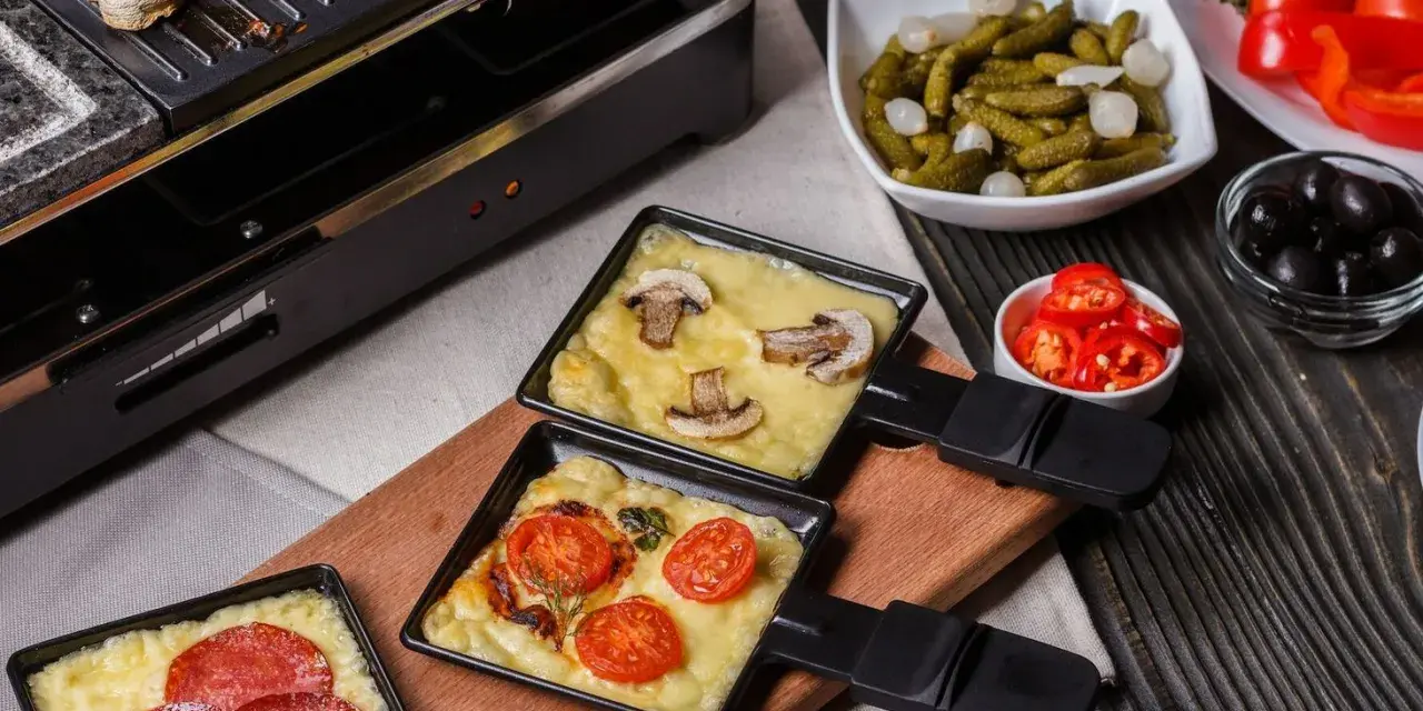 Raclette z pieczarkami i pomidorami, obok kiełbaski. Idealny ser do raclette rozpuszcza się w tych małych patelenkach.