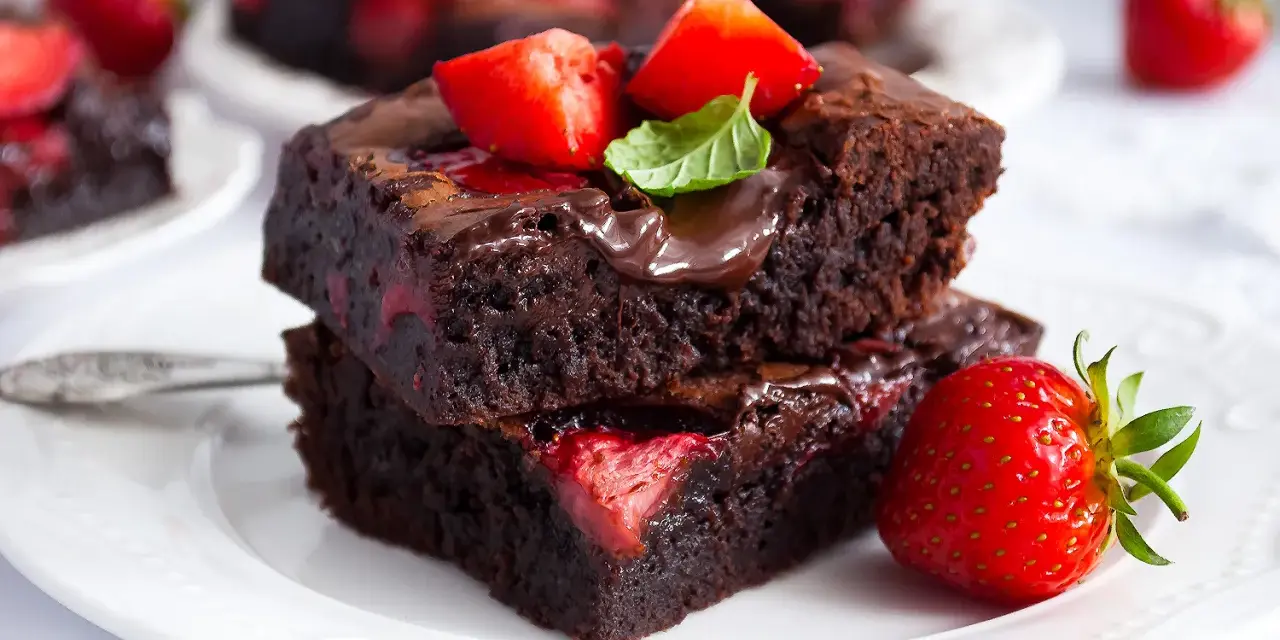 Pyszne brownie z truskawkami, polane czekoladą i ozdobione listkiem mięty. Idealne na deser.