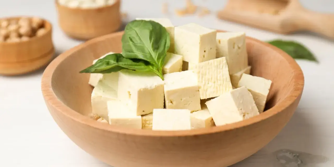 Kostki tofu w drewnianej misce z bazylią. Czy tofu można jeść na surowo? Tak, to idealny składnik do sałatek i przekąsek.