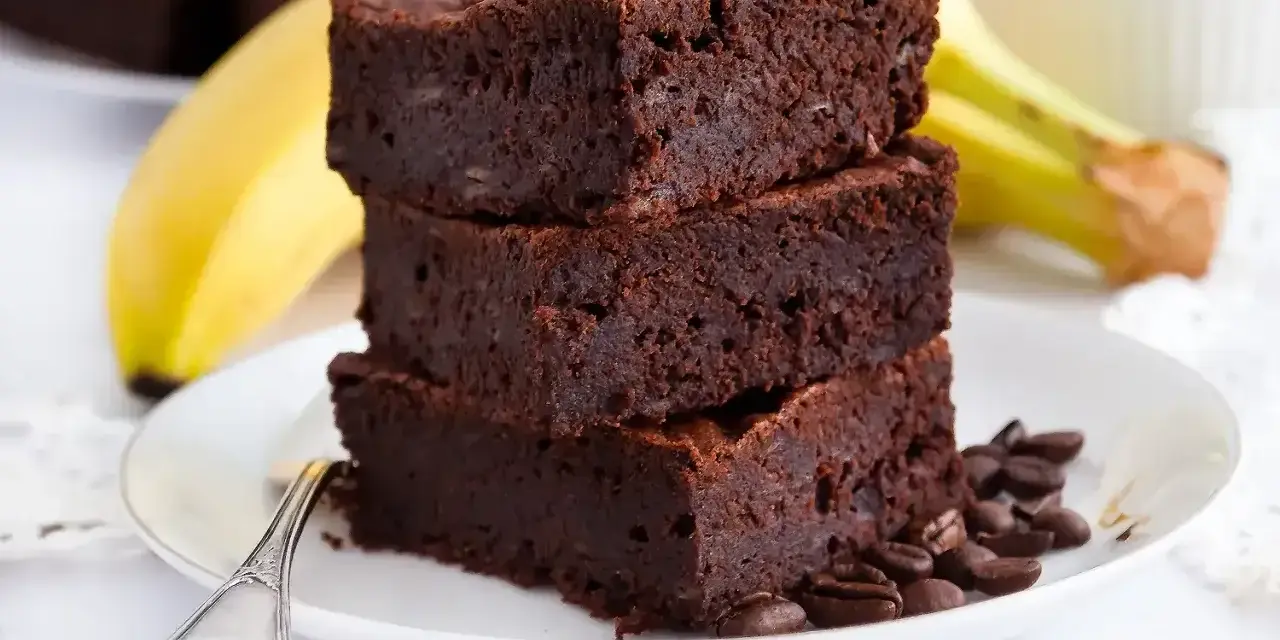 Stos puszystych brownie z bananami, ozdobiony ziarnami kawy, na talerzu z widocznym bananem w tle.