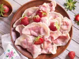Pyszne pierogi z truskawkami, ozdobione świeżymi owocami, wyglądają apetycznie na glinianym talerzu.
