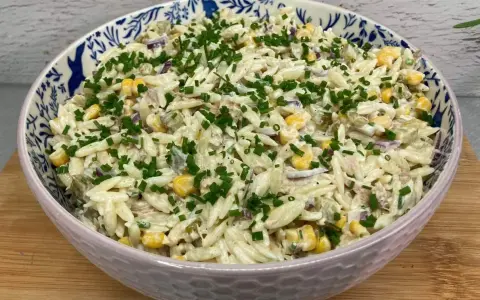 Pyszna sałatka z tuńczykiem i makaronem orzo, z kukurydzą i szczypiorkiem, w ozdobnej misce.