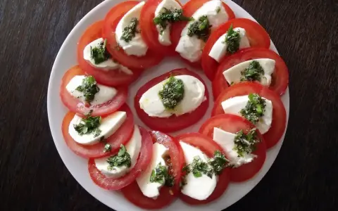 Pyszne pomidory z mozzarellą, ułożone na talerzu, posypane ziołami. Idealna przekąska na lato.