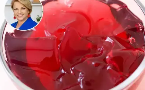 Kobieta w niebieskiej marynarce uśmiecha się obok miseczki z galaretką. Dowiedz się, ile tężeje galaretka, by cieszyć się deserem!