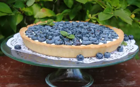 Pyszna tarta z borówkami, udekorowana listkiem mięty, prezentuje się apetycznie na szklanej paterze.