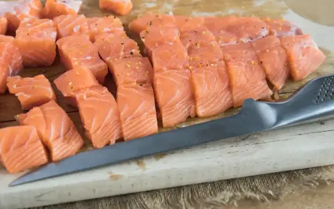 Pokrojony łosoś, idealny jaki łosoś do sushi, leży na desce obok noża.