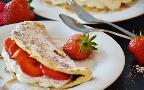 Słodki omlet z bitą śmietaną i truskawkami, posypany cukrem pudrem. Idealny przepis na deser.