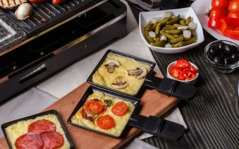 Raclette z pieczarkami i pomidorami, obok kiełbaski. Idealny ser do raclette rozpuszcza się w tych małych patelenkach.