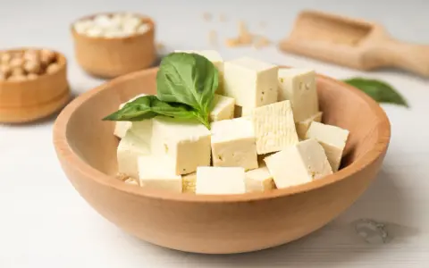 Kostki tofu w drewnianej misce z bazylią. Czy tofu można jeść na surowo? Tak, to idealny składnik do sałatek i przekąsek.
