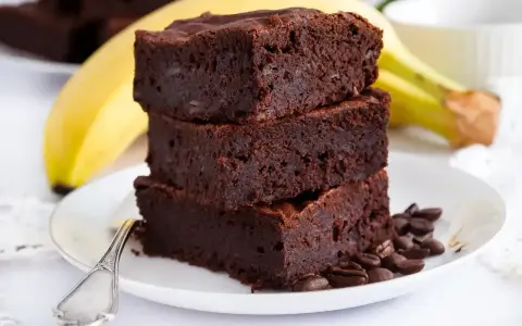 Stos puszystych brownie z bananami, ozdobiony ziarnami kawy, na talerzu z widocznym bananem w tle.