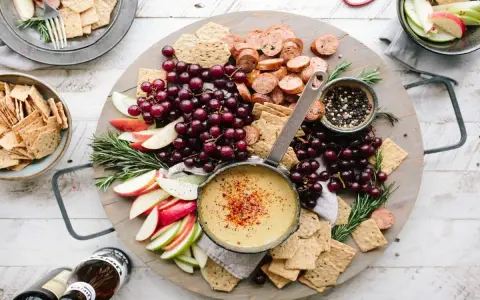 Idealne menu na sylwestra w domu: deska z serkiem, winogronami, jabłkami, kiełbaską i krakersami.