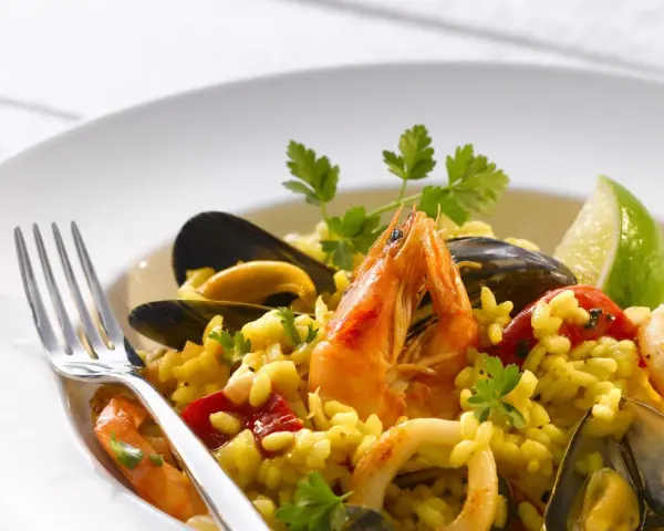 Pyszne risotto z owocami morza: krewetki, małże, kalmary i ryż, udekorowane natką pietruszki i ćwiartką limonki.