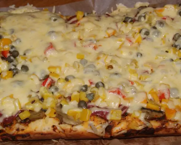 Pyszna pizza na grubym cieście z warzywami i roztopionym serem.