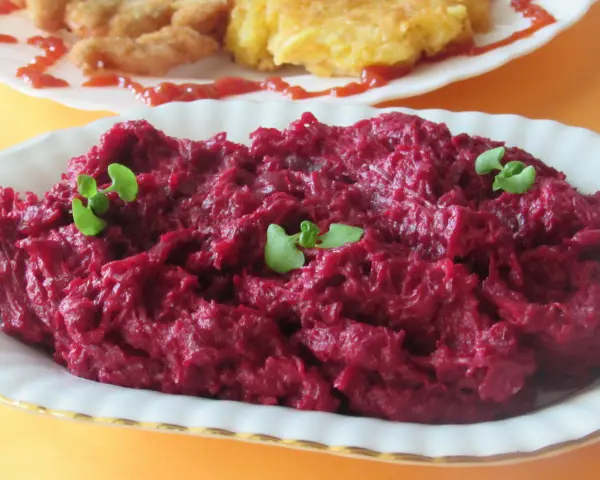 Pyszne, purpurowe buraczki na ciepło, udekorowane listkami ziół. Obok widać kotlety i placki ziemniaczane.