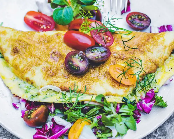 Złocisty omlet z cukinią, podany z kolorową sałatką i pomidorkami koktajlowymi. Pyszne i zdrowe śniadanie.