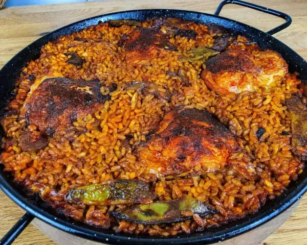 Pyszna paella z kurczakiem, ryżem i warzywami w tradycyjnej patelni.