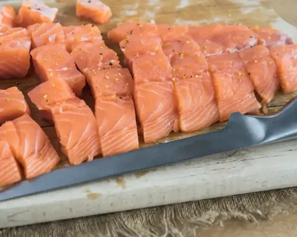 Pokrojony łosoś, idealny jaki łosoś do sushi, leży na desce obok noża.