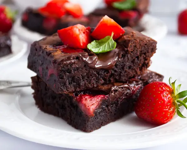 Pyszne brownie z truskawkami, polane czekoladą i ozdobione listkiem mięty. Idealne na deser.