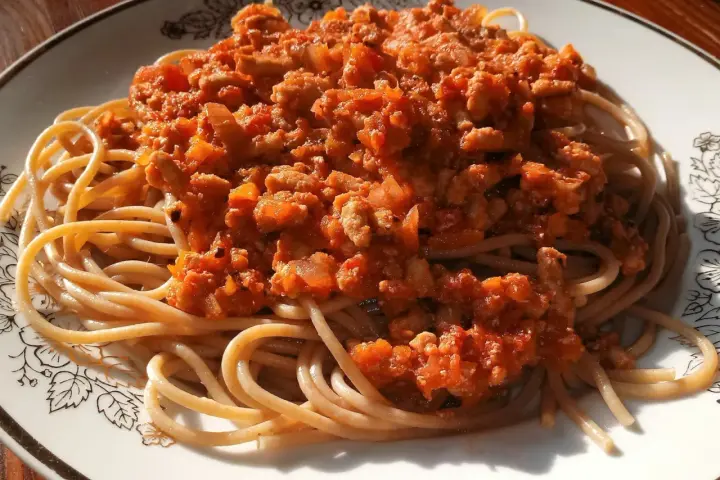 Porcja pysznego spaghetti bolognese z aromatycznym sosem mięsnym i pomidorowym, podana na talerzu z ozdobnym wzorem.