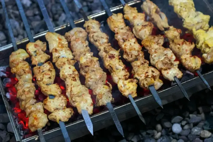 Aromatyczny kebab z kurczaka na rozżarzonych węglach. Soczyste kawałki mięsa pieką się na szpikulcach, tworząc apetyczny widok.