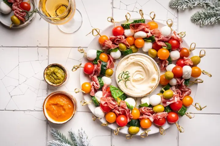 Kolorowe przystawki na zimno w kształcie wieńca, z mozzarellą, pomidorkami, oliwkami i salami, podane z dipami.